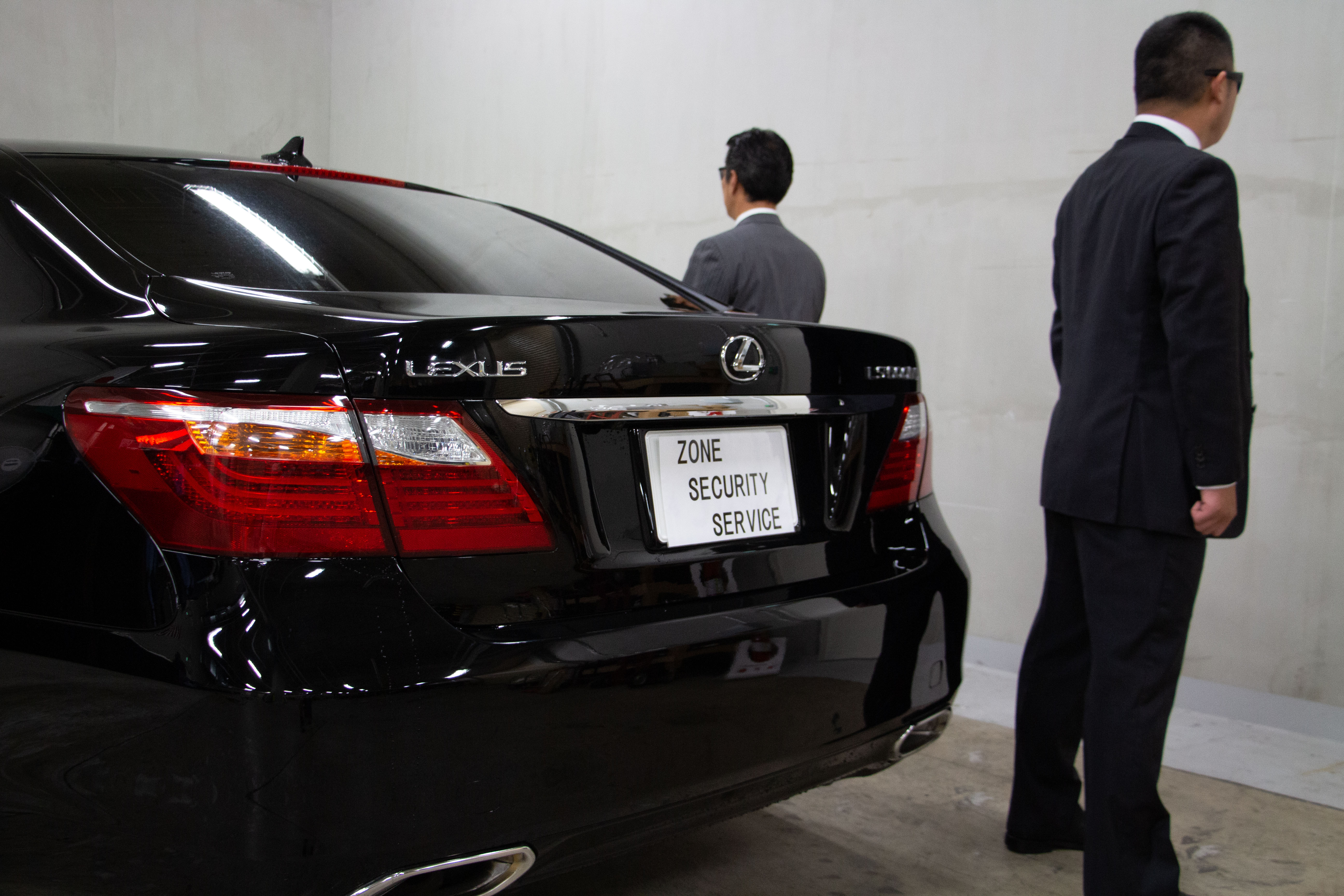 Suited Zone security personnel beside a black vehicle